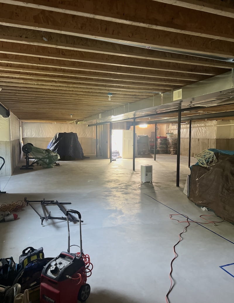 Unfinished basement with exposed joists, concrete floor, and construction equipment