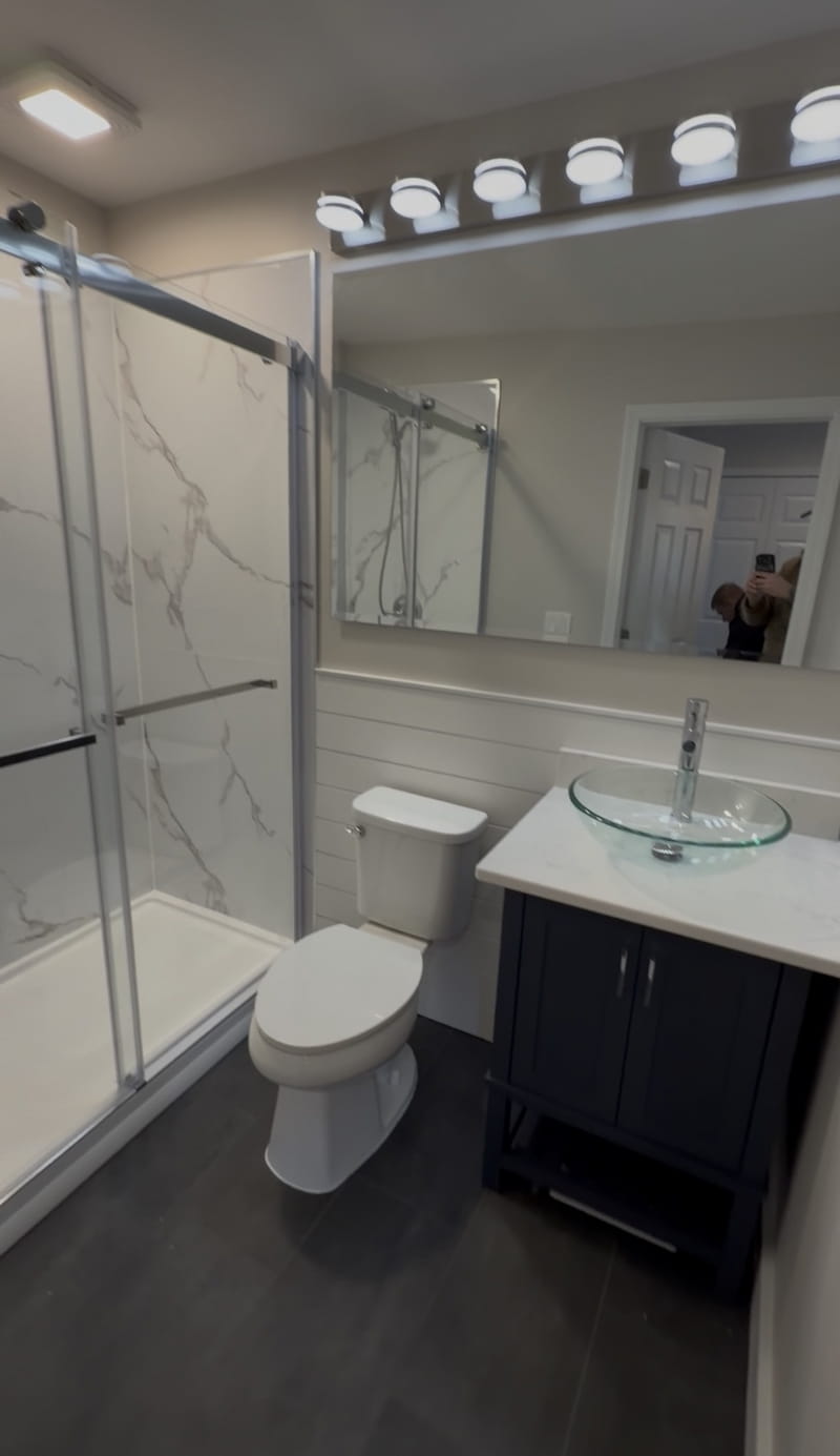 Spa-inspired bathroom remodel in Birmingham, Michigan — marble glass-door shower with dark vanity and glass vessel sink