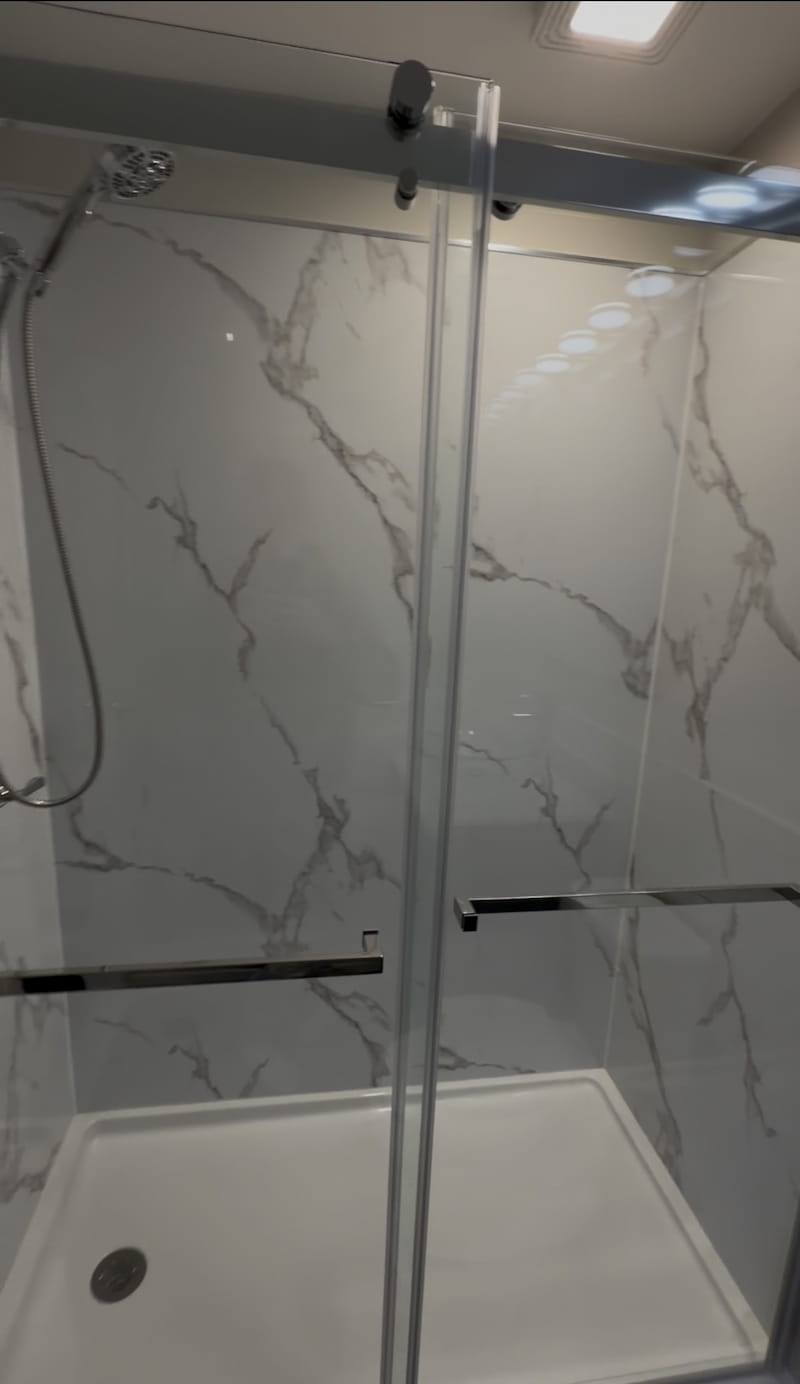 Close-up of frameless sliding glass shower door with marble-look surround