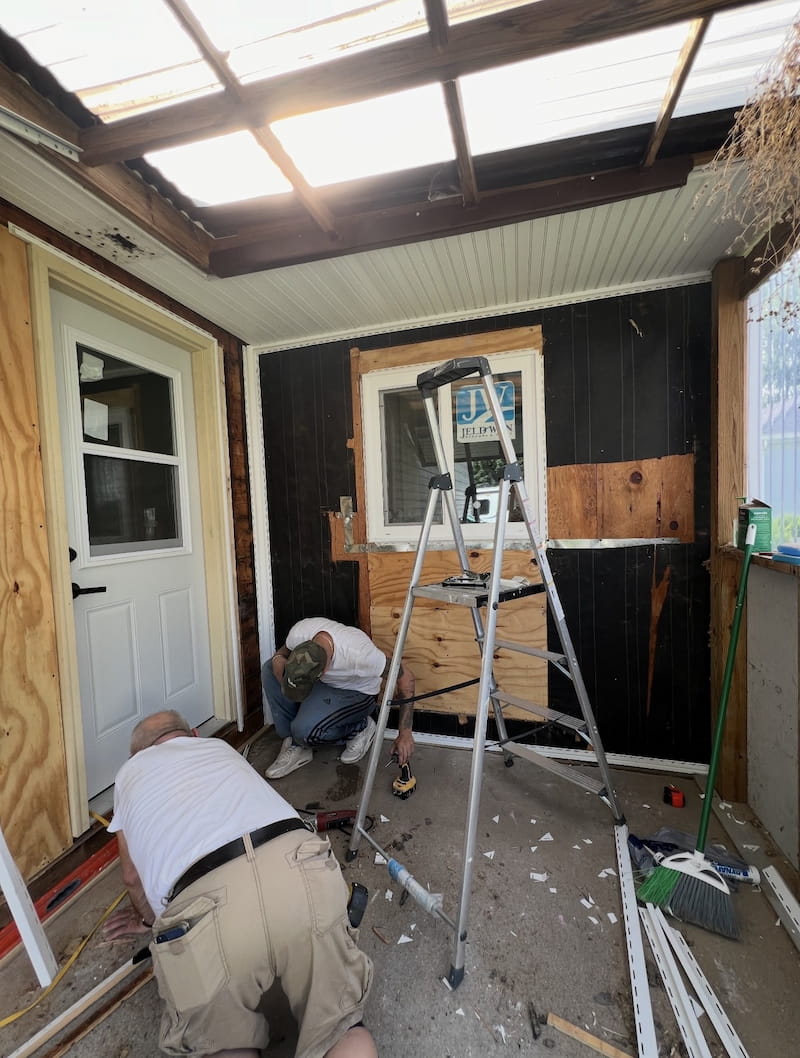 Porch renovation in progress — old walls removed, crew working with ladder and tools