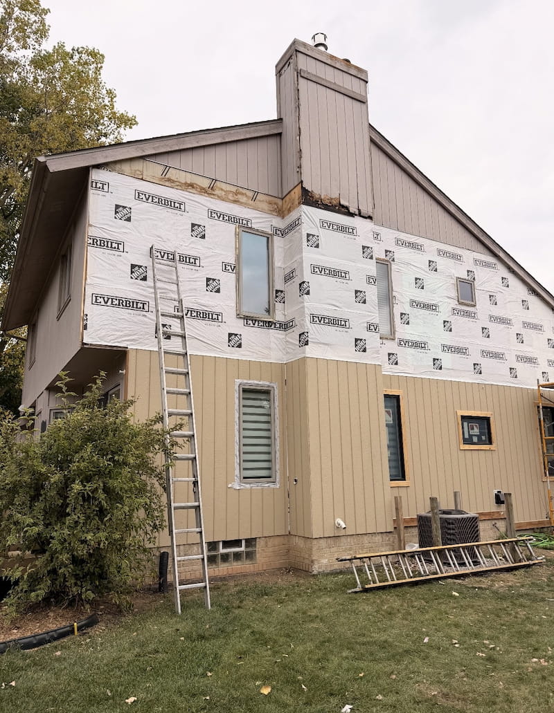 House mid-renovation with house wrap exposed, new siding being installed on lower half